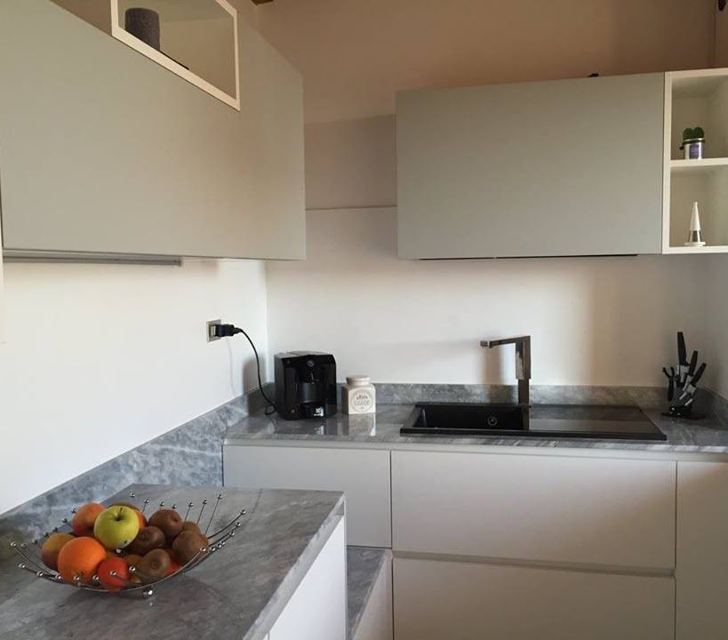 Cucina a Usago: zona lavello con top in pietra grigia e ante bianche